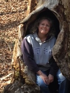 Photo of Bonnie sitting and smiling in a hollow tree trunk